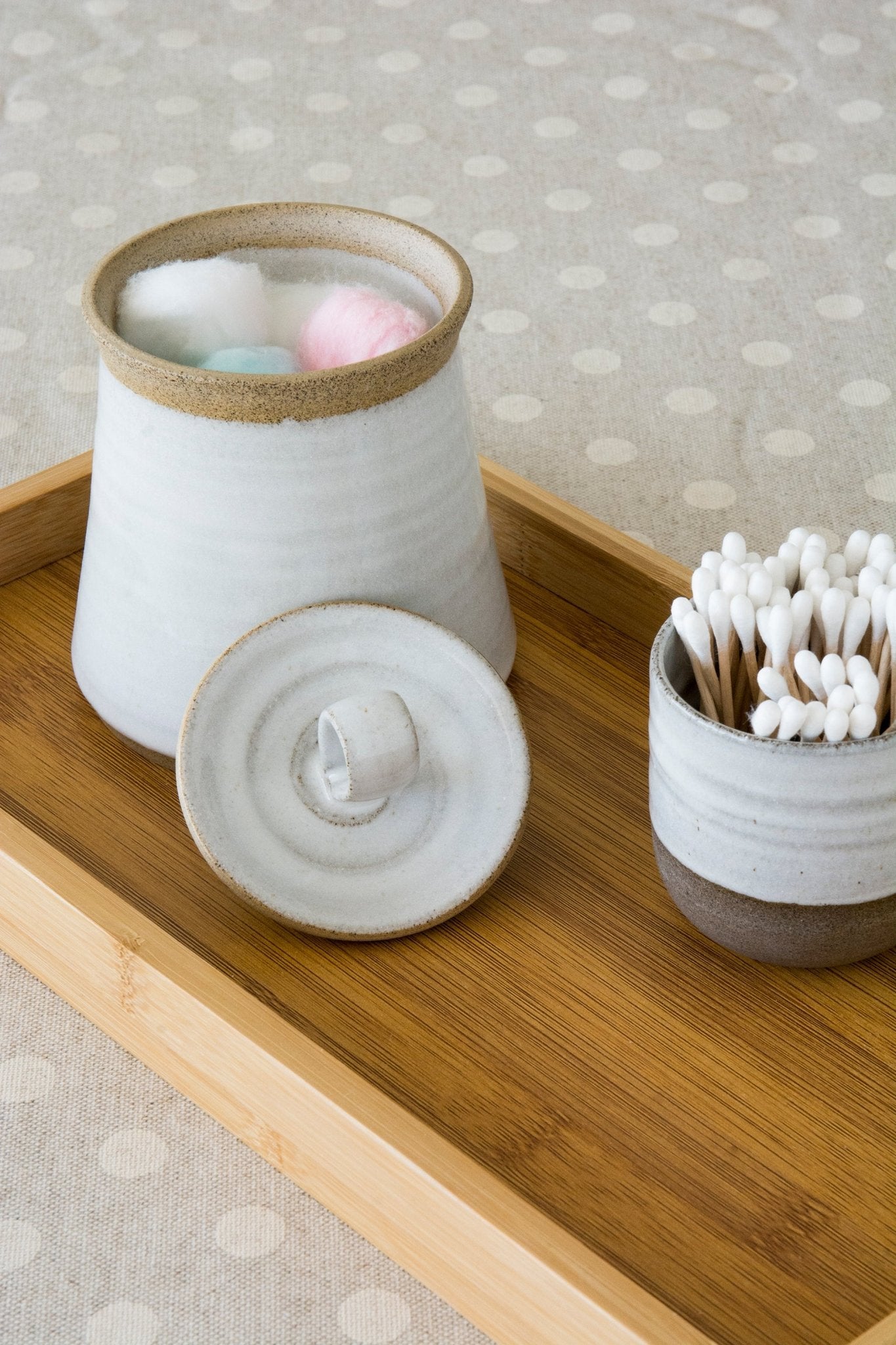 Sleek cylindrical pottery container in soft beige, displaying cotton swabs alongside farmhouse decor elements